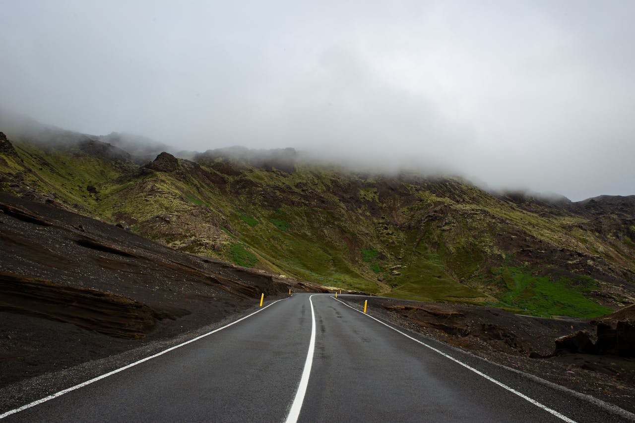 A foggy mountain road in Iceland, offering a serene travel scene with lush green hills.